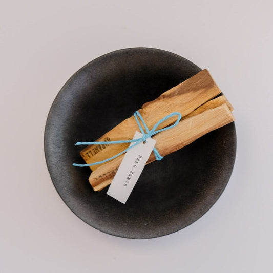 Palo Santo sticks tied with a blue ribbon on a black dish against a light gray background