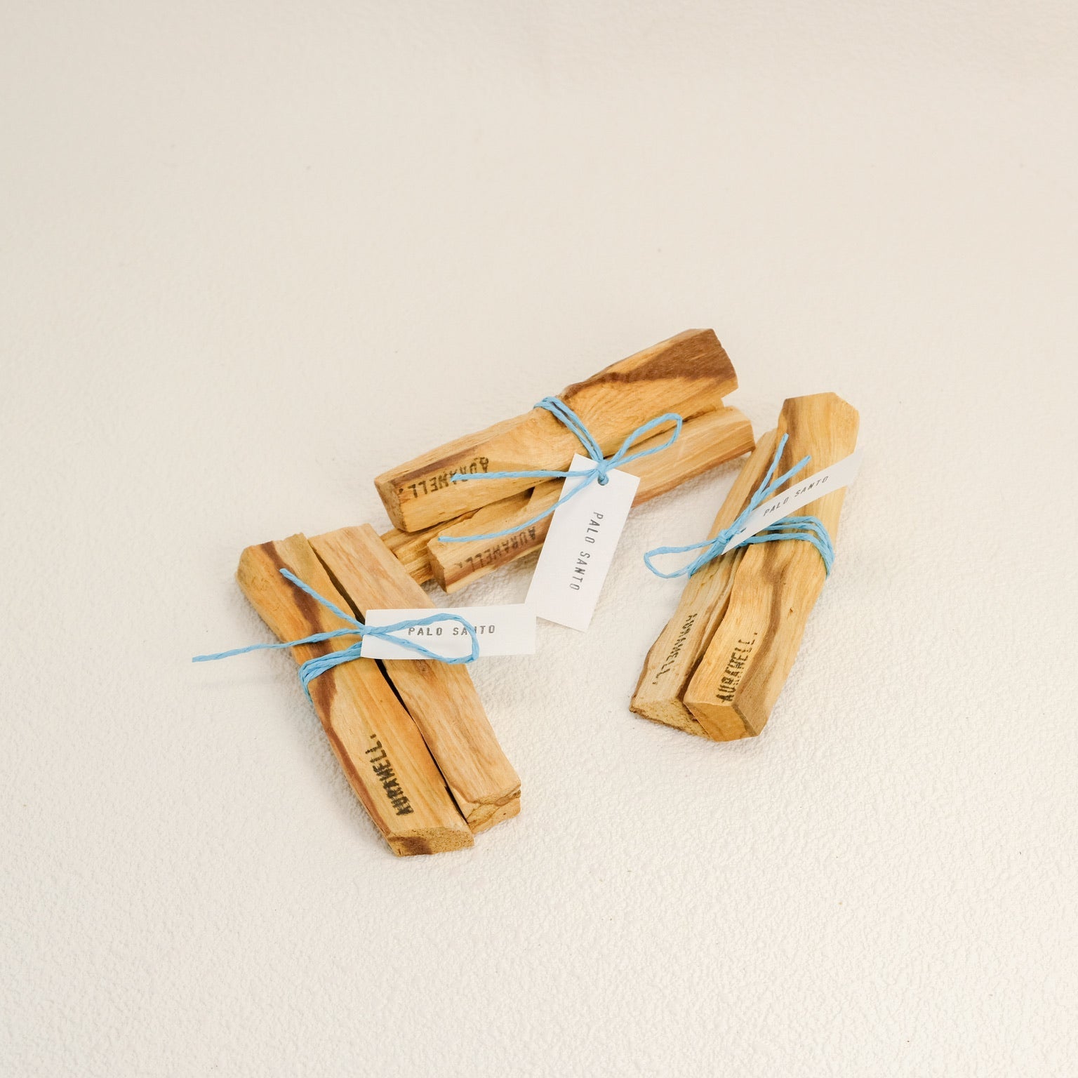 Three wooden incense sticks tied with blue string on a beige background